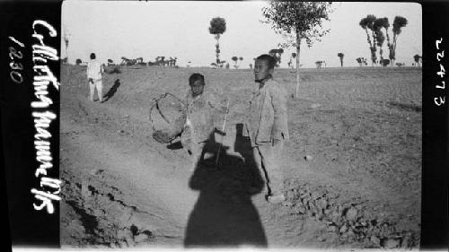 Children stand outside, with shadow of photographer between them