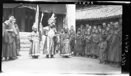 Crowd standing, watching procession of people in masks