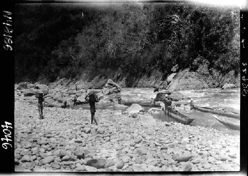 People carry things from boats along riverbank