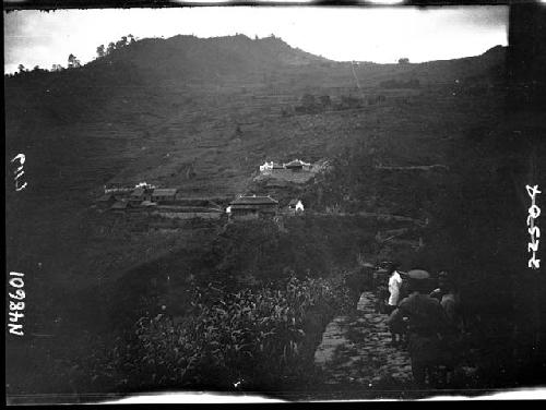 Hillside with buildings, with people walking along road in foreground