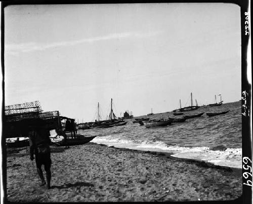 Person walking along beach, boats on water