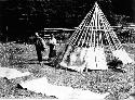 People standing by partially constructed teepee