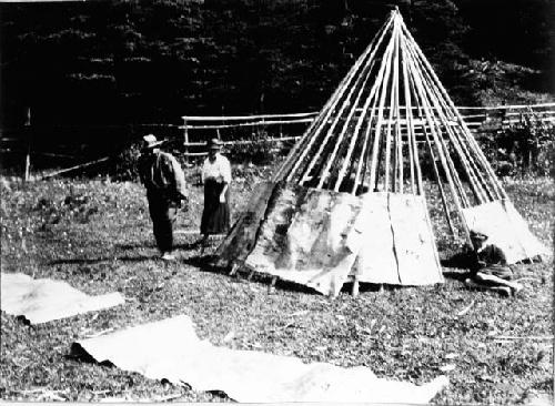 People standing by partially constructed teepee