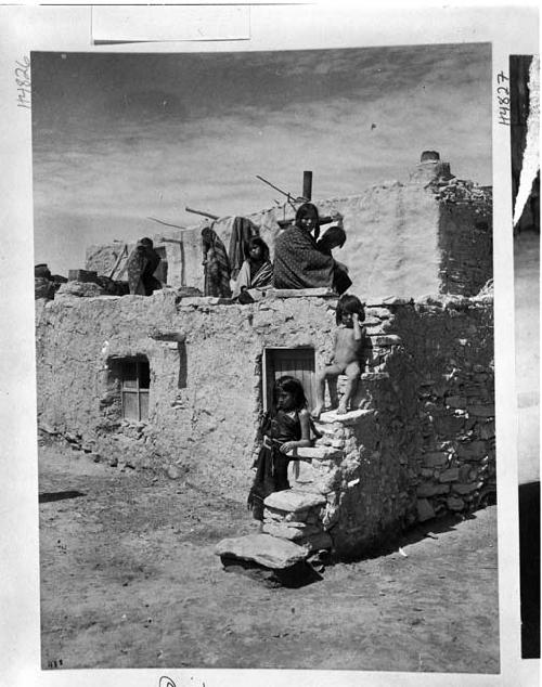 Hopi woman and children sitting and standing on pueblo roof and steps at Oraibi Pueblo