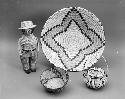 Large coiled bowl-shaped basket with flaring sides and yellow star motif; coiled globular basket with movable handle, attached lid and flower motif; coiled basketry figure of a man with detachable hat; coiled cattail reed olla bowl with lizard motif.