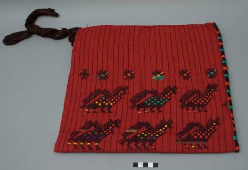 Headcloth, two panels sewn together, red ground with thin black stripes, brocaded burgundy animal forms, four burgundy corner tassels. Thin wood shavings are still attached to tassels (possibly a packing material).