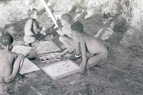 Four boys painting with Western materials, including /Gishay (son of "Old Gau"), with his foot bandaged, /Gao (son of "Old Gau") wearing a shirt, and Tsamgao (≠Toma's son), wearing a feather in his hair