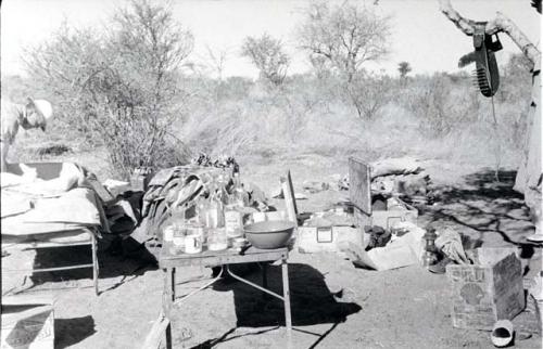 Claude McIntyre leaning over a cot next to his belongings in the expedition camp