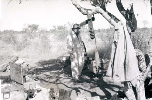 Laurence Marshall standing in the expedition camp next to a cartridge belt hanging from a tree