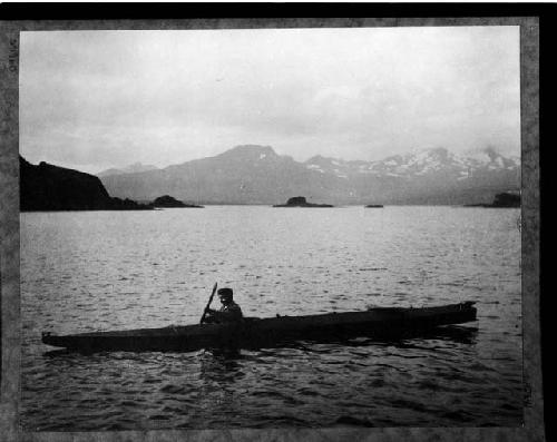 Aleut man in kayak with mountains in the background

