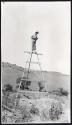 Scan of page from Judge Burt Cosgrove photo album.  On ladder taking photograph of excavations.