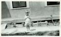 Scan of page from Judge Burt Cosgrove photo album.  Child standing in front of building.