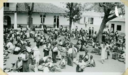 Scan of photograph from Judge Burt Cosgrove photo album.Market at Santiago de Atitlan Woman's dress-bright red shirt-white huipil-red strip across right shoulder-long narrow bank wound the head to form a halo