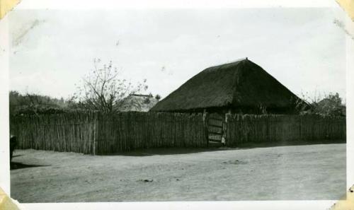 Scan of photograph from Judge Burt Cosgrove photo album.Thatched roof and cane fence-Santa Maria de Jesus