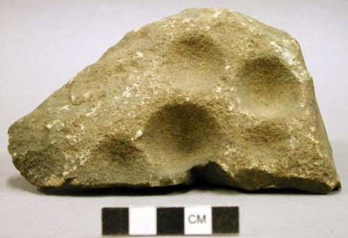 Ground stone,  large pits on one surface.