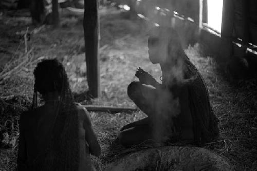 Samuel Putnam negatives, New Guinea;  2 women as they sit doing little work; smoke rises from the fire