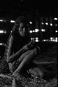 Samuel Putnam negatives, New Guinea; woman sitting in a hunu works with her hands; she looks at camera