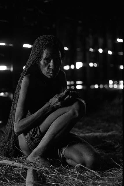 Samuel Putnam negatives, New Guinea; woman sitting in a hunu works with her hands; she looks at camera