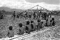 Samuel Putnam negatives, New Guinea;  RC mission putting up a school at Kibit Silimo;  Dani sitting on the lumber in foreground;  building in background.