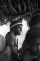 Samuel Putnam negatives, New Guinea; man squats under an olea; seen between other figures