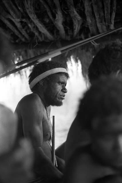 Samuel Putnam negatives, New Guinea; man squats under an olea; seen between other figures