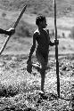 Samuel Putnam negatives, New Guinea; Kusa, who has been working in the field, stands on his foot holding a large digging stick in his hand