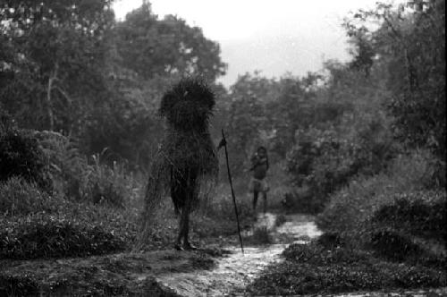 Samuel Putnam negatives, New Guinea; a woman with her grass raincoat on walking towards her village in Abulupak; a young girl walking in the opposite direction