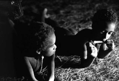 Samuel Putnam negatives, New Guinea; both  boys; Uwar and Yege Abu; lying on the ground on the straw in the honai