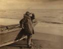 Inuit man leaning against a boat and looking out to sea