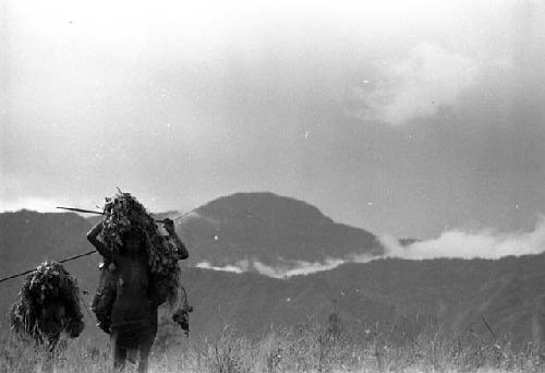 Samuel Putnam negatives, New Guinea; two wolem walking with enormous loads framed against a misty sky