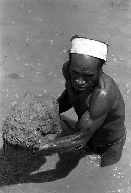 Samuel Putnam negatives, New Guinea; Siluk clearing a ditch; about to heave an enormous piece of mud up onto the side