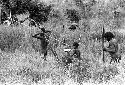 Samuel Putnam negatives, New Guinea; warrior walking in the grass near the Tokolik; expedition member in far left bkgd