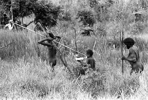 Samuel Putnam negatives, New Guinea; warrior walking in the grass near the Tokolik; expedition member in far left bkgd