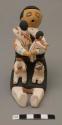 Storyteller figure with four children, two in arms, two on lap; one lap child holding pot; signed T. Decora / Cochiti, N. M. Also corn and rain? symbols