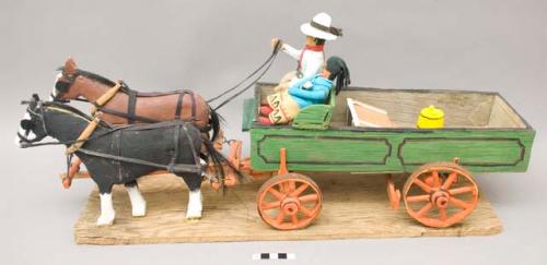 Folk art wagon pulled by two horses, carrying Native couple with baby, on plywood base; brown horse detached from base; left back wheel detached from base.