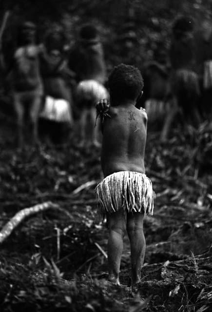 Samuel Putnam negatives, New Guineal; little girl stands in frgd in focus; dancers completely out of focus in the bkgd