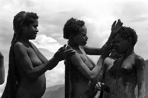 Samuel Putnam negatives, New Guinea; 2 women and 1 girl putting on clay