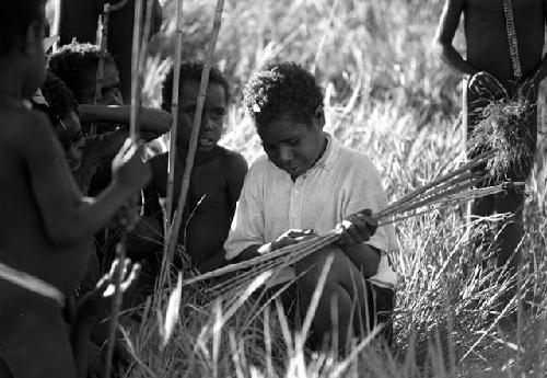 Samuel Putnam negatives, New Guinea; Etai; little boys including Uwar surround another little boy in a white shirt and blue pants who is investigating someone's bow and arrows