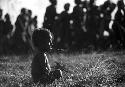 Samuel Putnam negatives, New Guinea; little boy sits on the grass behind the dancers
