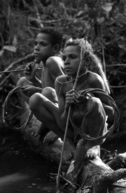 Samuel Putnam negatives, New Guinea; Okal and Isile perched on a log near the Elokhere River; equipped to play sikoko wasin; these are twin boys