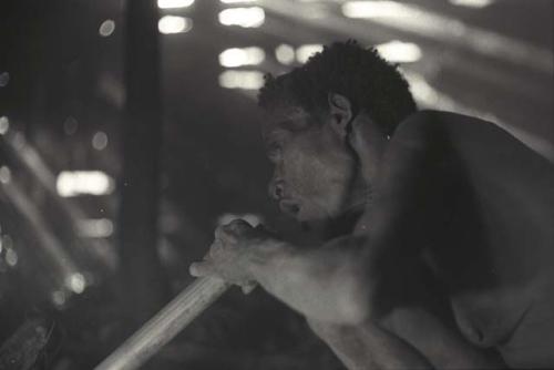 Samuel Putnam negatives, New Guinea; Aneake blowing thru a large bamboo pipe to get the fire going