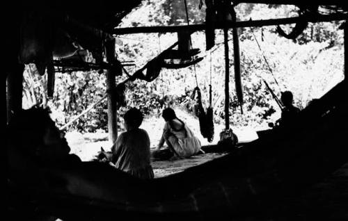 Interior of Carib house -- men lying in hammock, women making cassava bread