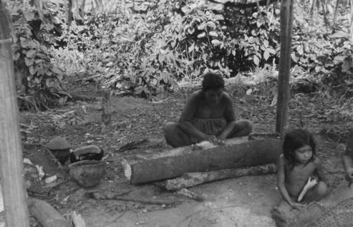 Woman grating cassava on the tin grater into the bark trough