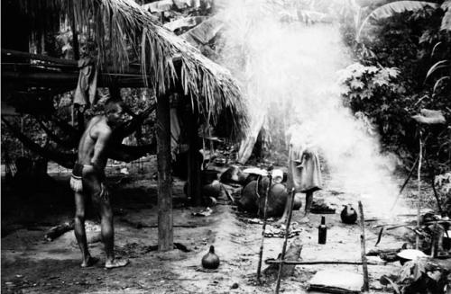 Breakfast at a Carib house. Babracote for drying meat over fire at right & hammocks slung in house interior.