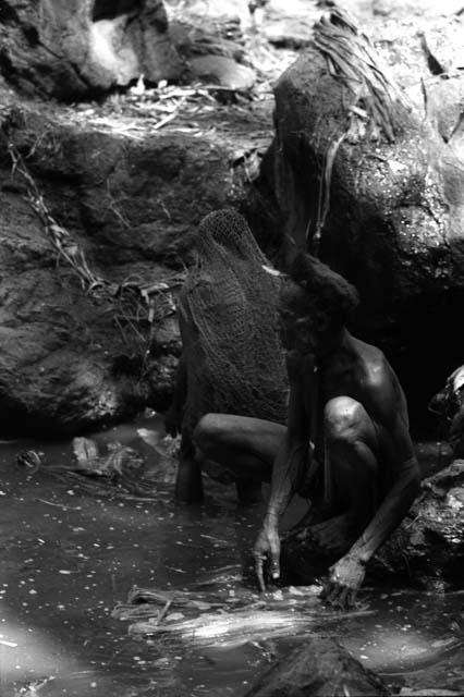 Ilueaima ('Kurelu Salt Well'). man sits on rock retrieving trunk from pool.