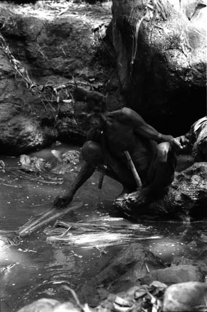 Ilueaima ('Kurelu Salt Well'). man sits on rock retrieving trunk from pool.