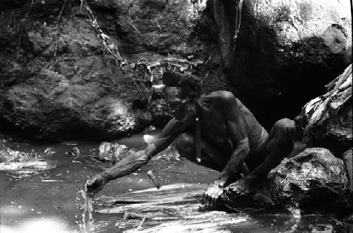 Ilueaima ('Kurelu Salt Well'). man sits on rock retrieving trunk from pool.