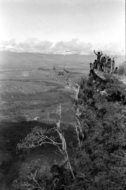 Kids on promontory above mountain wall, shout into Valley with raised arms