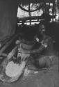 Woman mashing cassava with wooden pestle in trough