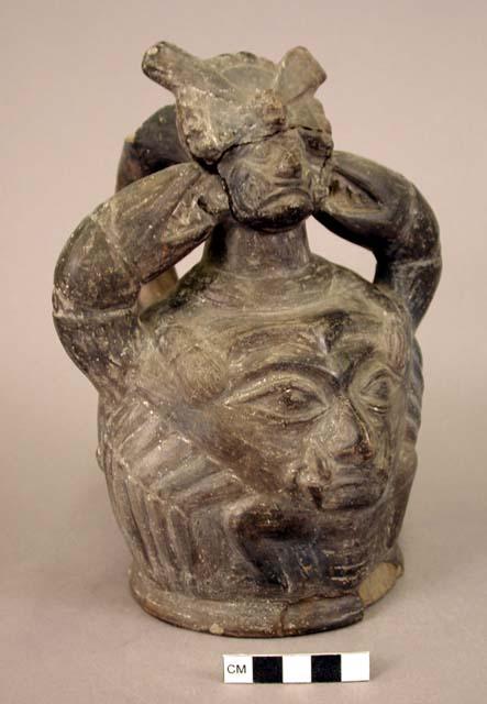 Ceramic bottle, stirrup spout, zoomorphic design, molded human face and crown